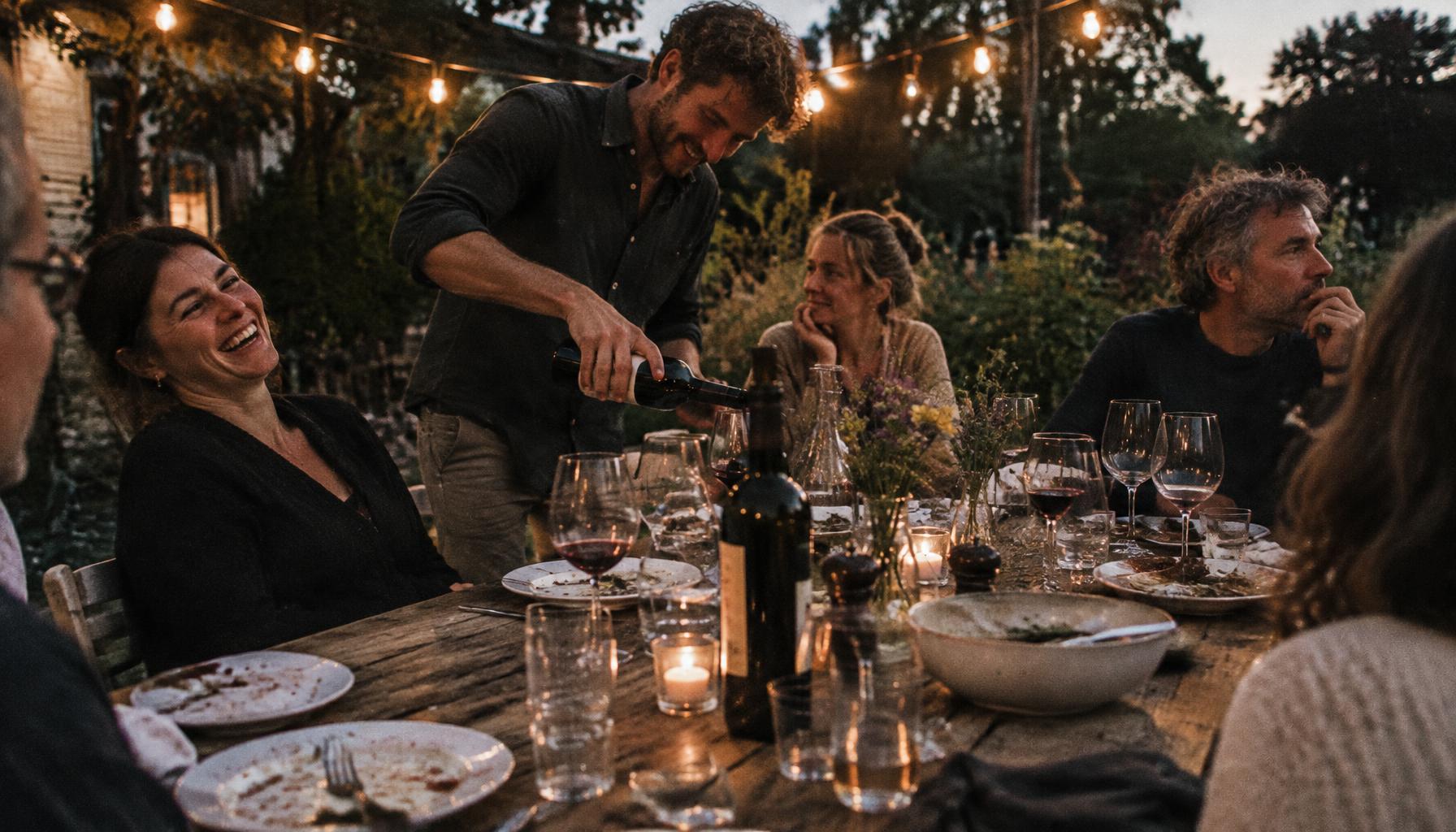 Runde mit Freunden am Gartentisch im Abendlicht – Lachen und stille Momente nebeneinander